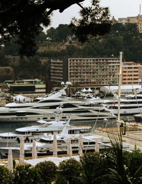 monaco-gp-harbour-luxury-yachts Luxury mega yachts docked in Monaco's Port Hercules, framed by Mediterranean greenery and iconic Monte Carlo architecture during the Monaco GP Fashion 2026 showcase.