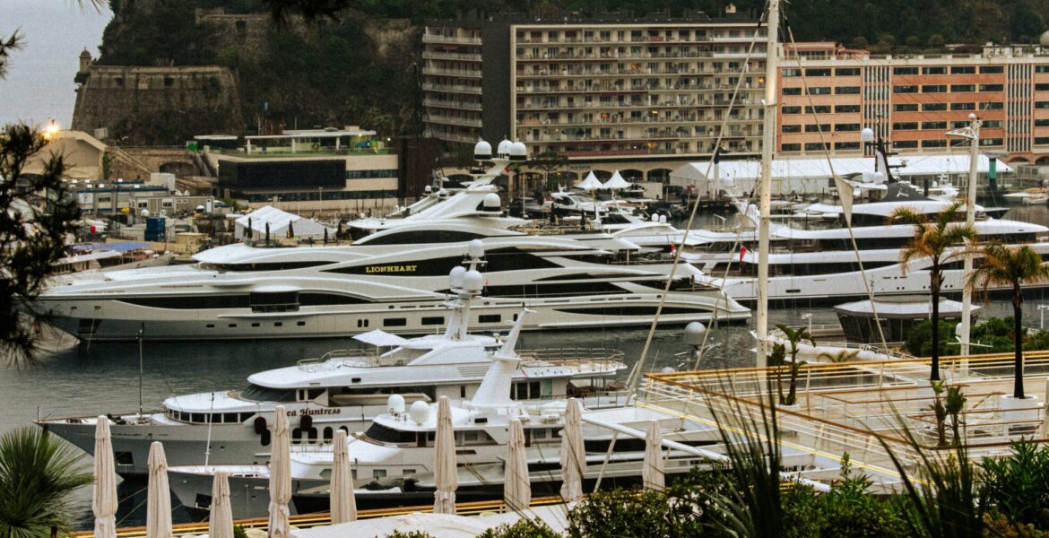 Luxury mega yachts docked in Monaco's Port Hercules, framed by Mediterranean greenery and iconic Monte Carlo architecture during the Monaco GP Fashion 2026 showcase.
