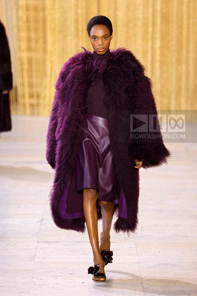 Model on the runway at the Akris fashion show in Paris, Fall Winter 2026 Ready To Wear Fashion Week, Runway Look #16 - Akris Fall/Winter 2026 runway look featuring a deep purple textured coat, turtleneck, and leather midi skirt.