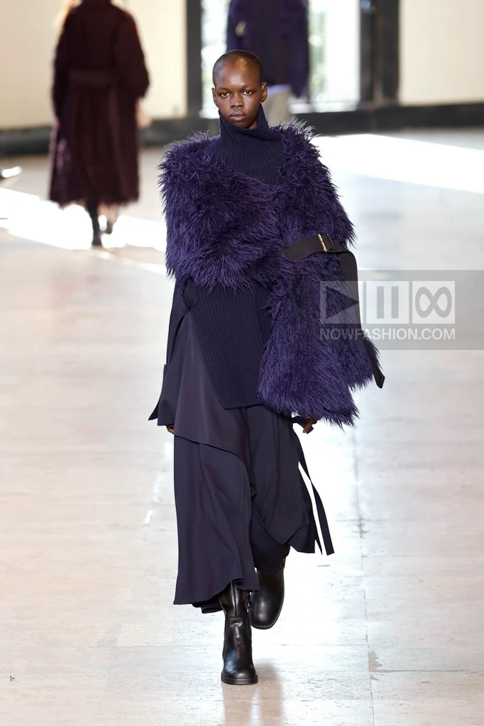 Model on the runway at the Ujoh fashion show in Paris, Fall Winter 2026 Ready To Wear Fashion Week, Runway Look #020 - CFCL Fall/Winter 2026 runway look featuring an asymmetrical deep purple draped knit dress.
